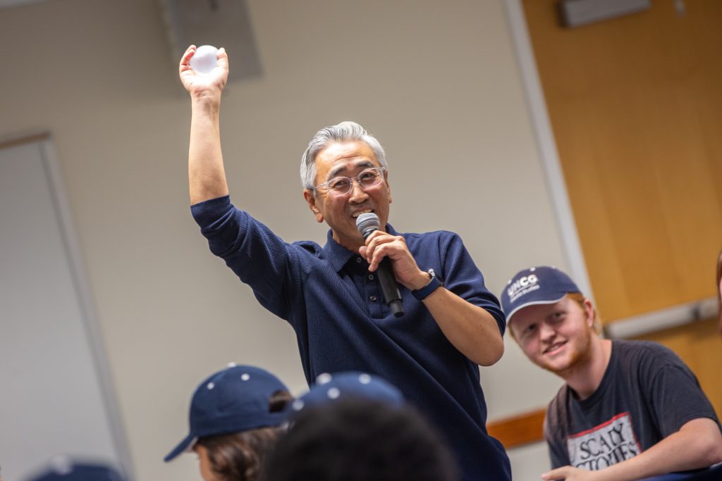 Department Head Changhee Chun standing up with a microphone and speaking to the group.