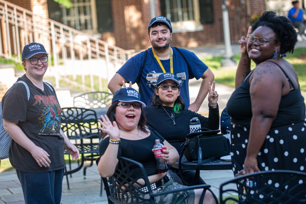 a group of UNCG Media Studies students smile as they gather around a table outside.